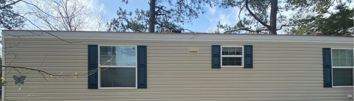 Beige house siding and dark shutters after a house wash, with clean white skirting below the windows.