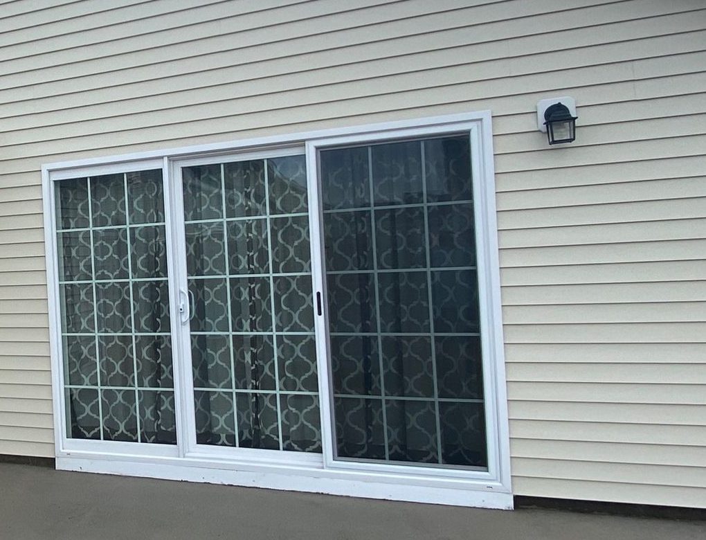 Clean beige vinyl siding and a white-framed sliding glass door after washing.