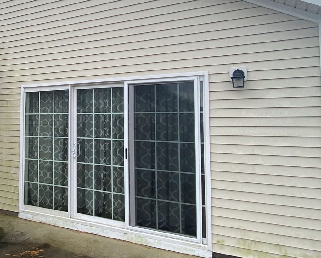 Beige vinyl siding and a white sliding door with green algae along the lower wall, before washing.